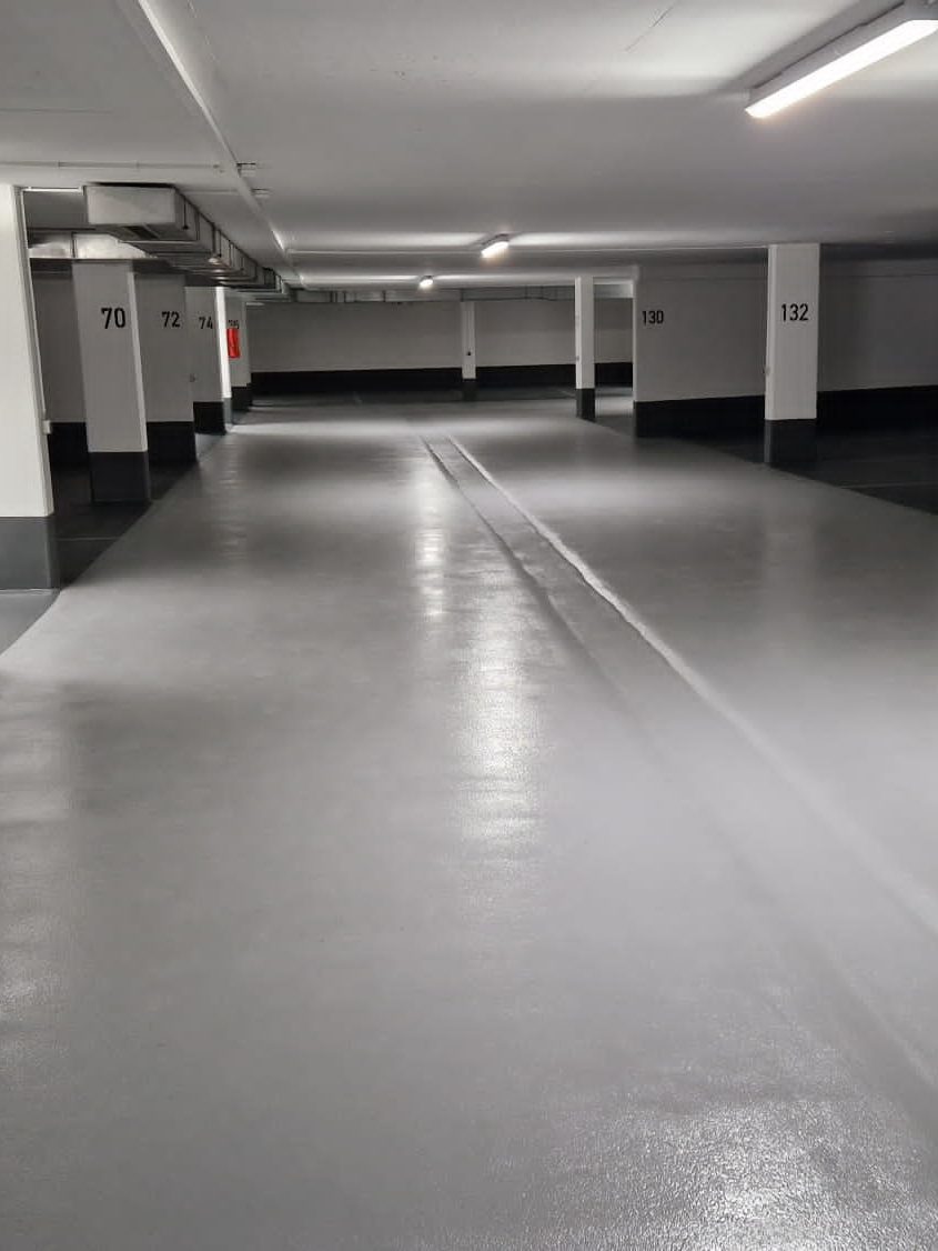 Leere Parkgarage mit grauem Boden und weißen Linien, gut beleuchtet.